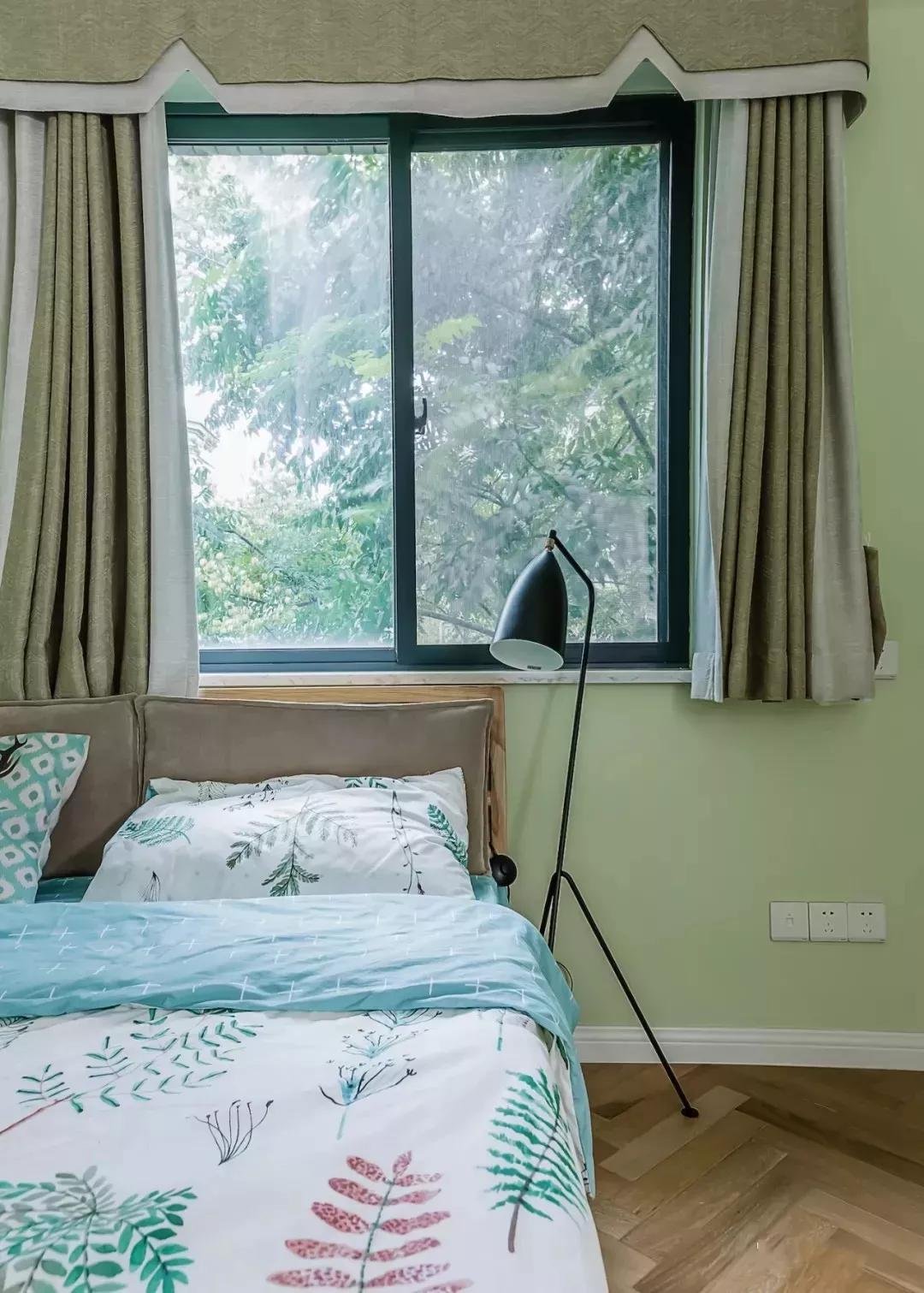次卧的床靠着窗户摆放,以绿色作为主色调,搭配带有绿植花纹的床品